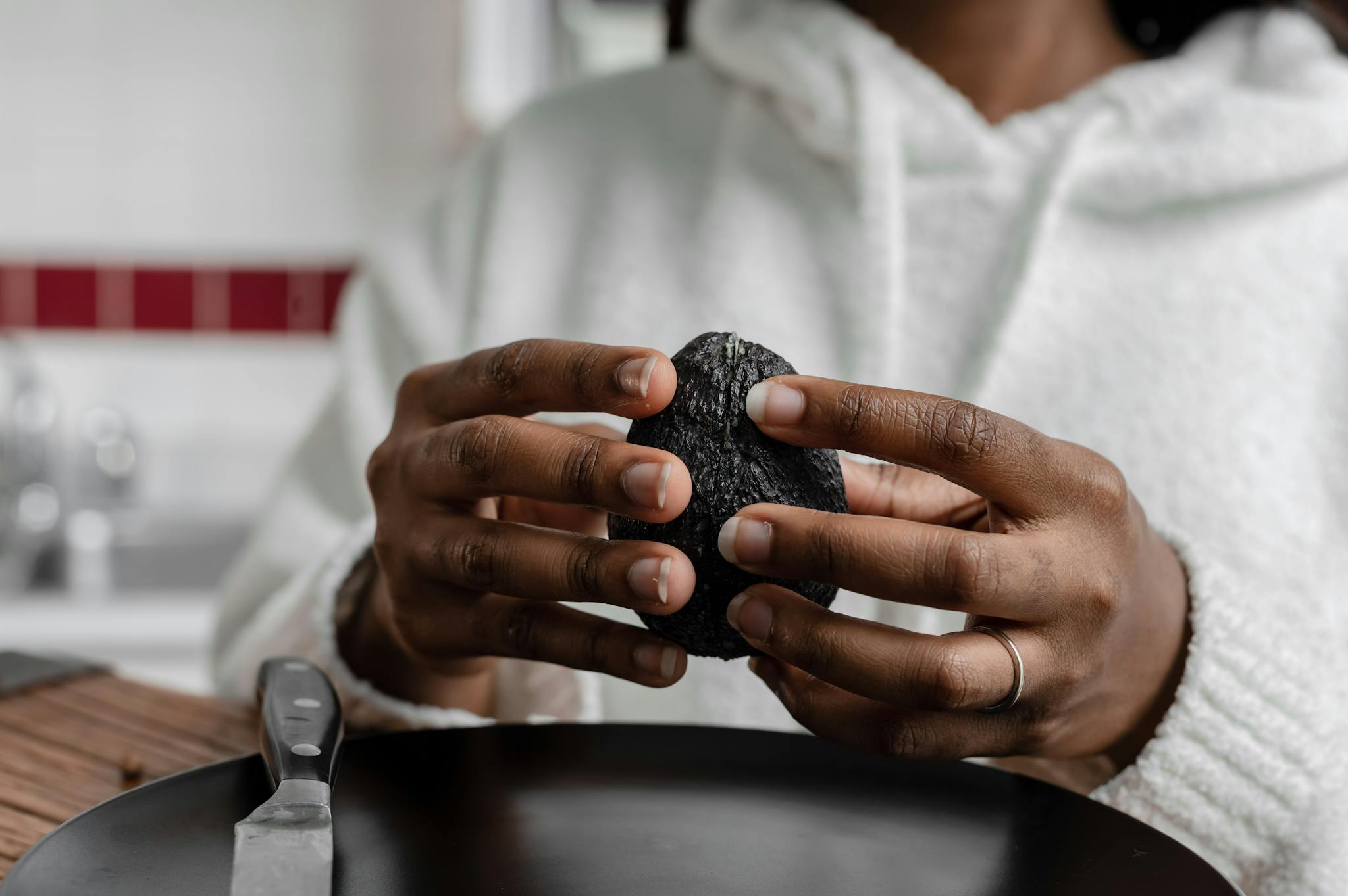 Hands holding a ripe avocado in a kitchen setting. Perfect for nutrition and cooking themes.